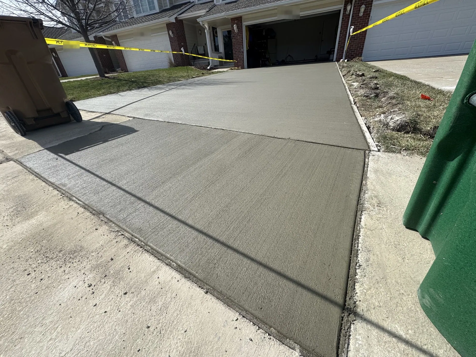 New concrete driveway approach leading up to a garage, freshly finished and taped off.