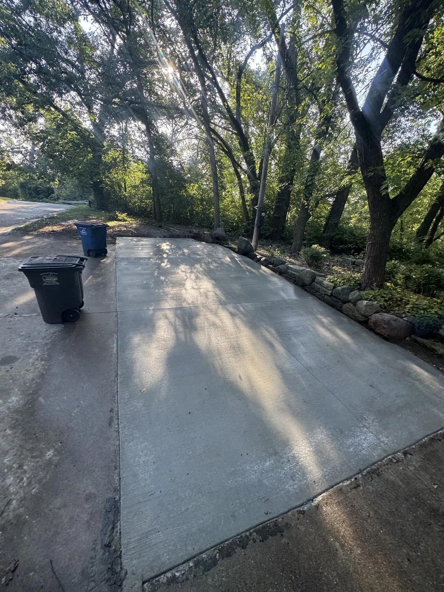 Finished concrete pad under trees beside a house.