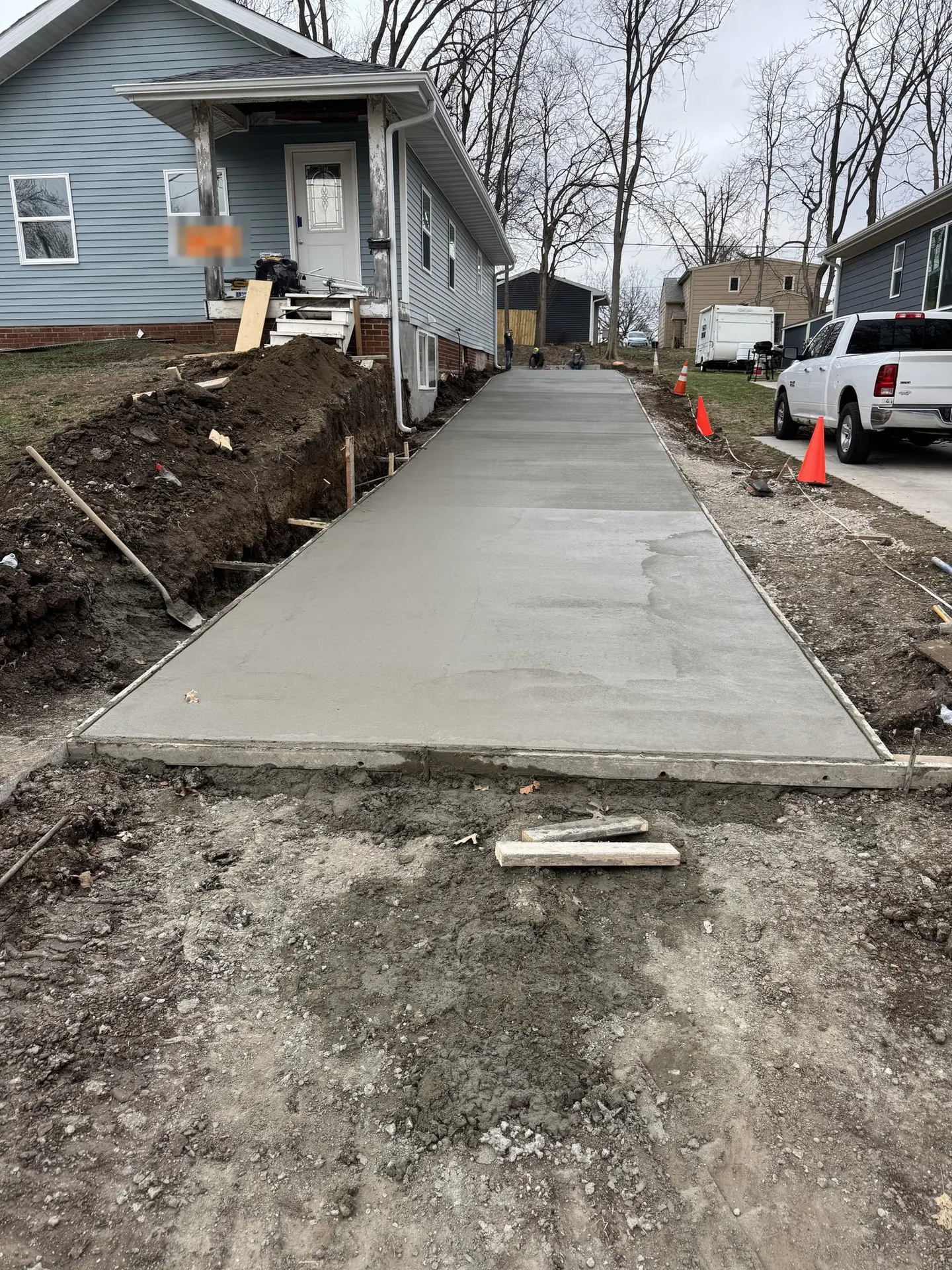 Long concrete walkway along a blue house, poured and being finished.